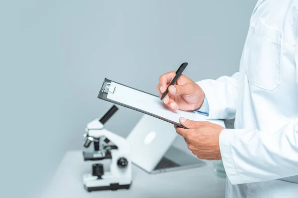 Cropped image of scientist writing something at clipboard isolated on white — Stock Photo
