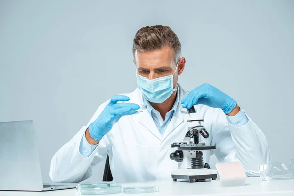 Gutaussehender Wissenschaftler in medizinischer Maske und medizinischen Handschuhen, der Experimente isoliert auf weißem Grund durchführt — Stockfoto