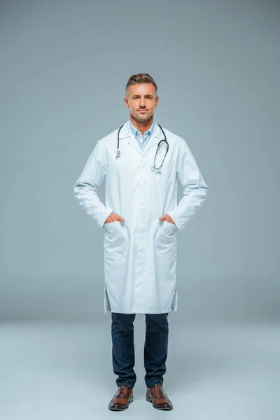 Beau médecin avec stéthoscope regardant la caméra sur gris — Photo de stock