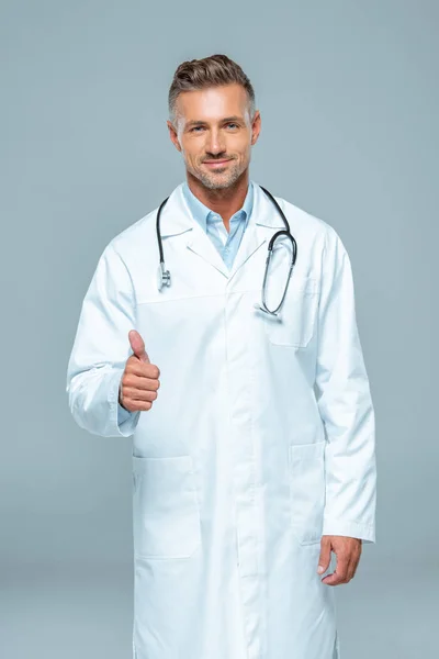 Beau médecin avec stéthoscope montrant pouce vers le haut et regardant la caméra isolée sur blanc — Photo de stock