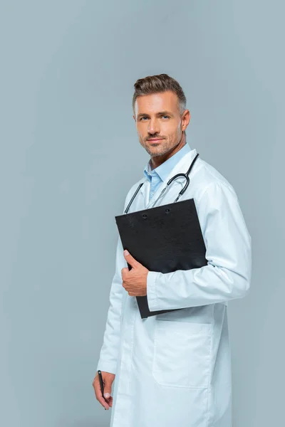 Красивый врач со стетоскопом и планшетом, смотрящий на камеру, изолированную на сером — стоковое фото