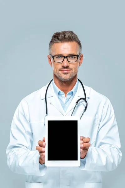 Guapo médico con estetoscopio mostrando tableta con pantalla en blanco y mirando a la cámara aislada en blanco - foto de stock
