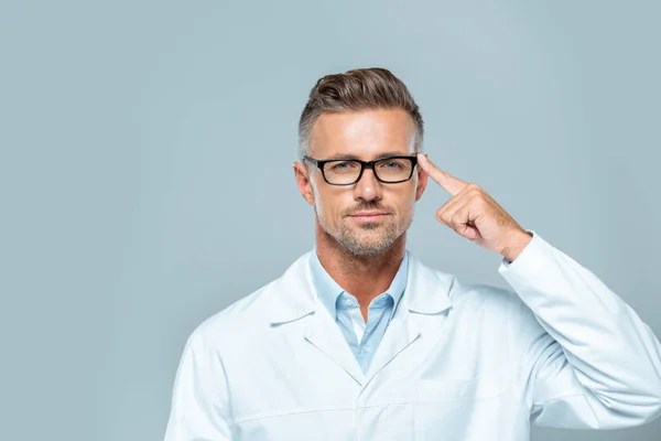 Guapo científico con gafas apuntando a su cabeza y mirando a la cámara aislada en gris, concepto de inteligencia artificial - foto de stock