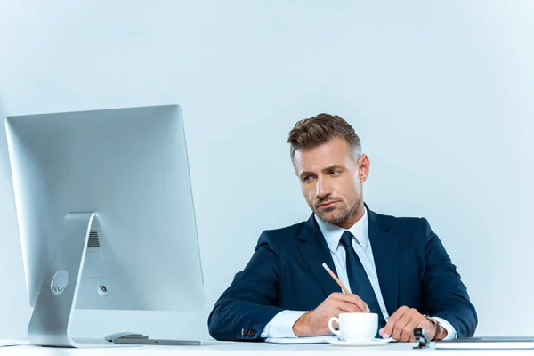 Красивий бізнесмен дивиться на комп'ютер за столом ізольовано на білому — стокове фото