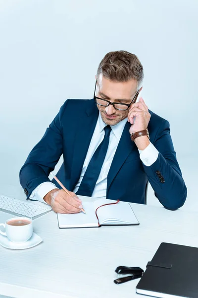 Hochwinkelaufnahme eines gutaussehenden Geschäftsmannes, der etwas schreibt und mit dem Smartphone spricht, isoliert auf Weiß — Stockfoto