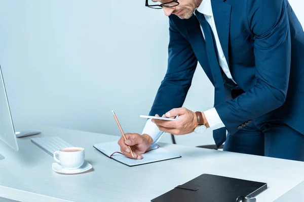 Abgeschnittenes Bild eines Geschäftsmannes, der auf sein Smartphone schaut und etwas Isoliertes auf Weiß schreibt — Stockfoto