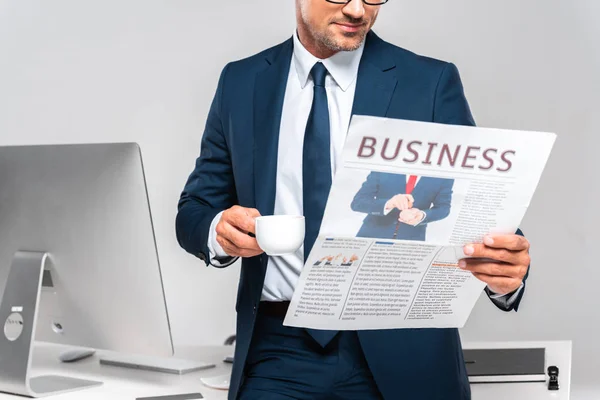 Cropped image of businessman holding cup of coffee and reading business newspaper isolated on white — Stock Photo