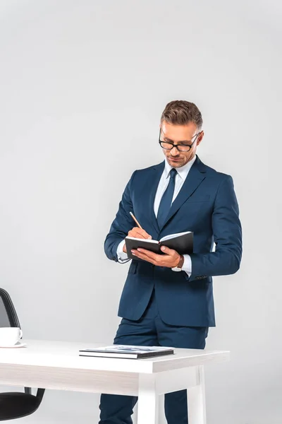 Guapo hombre de negocios escribiendo algo en cuaderno aislado en blanco - foto de stock