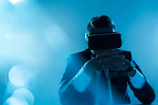 Businessman in virtual reality headset sitting isolated on blue, artificial intelligence concept — Stock Photo