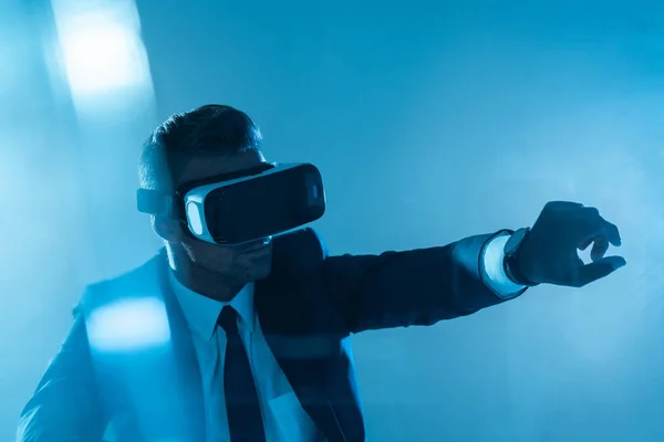 Бизнесмен в наушниках виртуальной реальности, касающихся чего-то изолированного на синем, искусственном интеллекте — стоковое фото