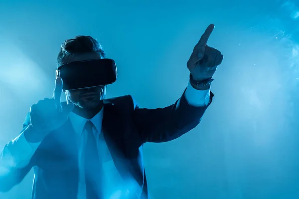 Businessman in suit and virtual reality headset touching something isolated on blue, artificial intelligence concept — Stock Photo