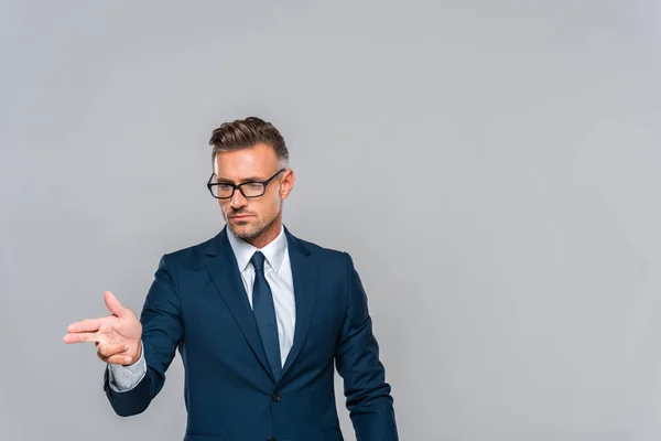 Gutaussehender Geschäftsmann mit Brille zeigt auf etwas Isoliertes auf grauem, künstlichem Intelligenzkonzept — Stockfoto