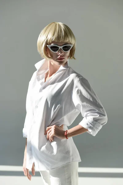 Jolie femme blonde en lunettes de soleil et tenue blanche à la mode debout avec akimbo main sur blanc — Photo de stock