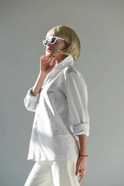 Vue à angle bas de jolie femme blonde en lunettes de soleil et tenue blanche à la mode regardant loin isolé sur blanc — Photo de stock