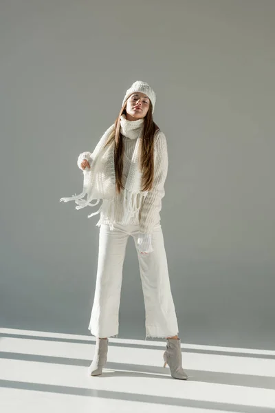 Привлекательная женщина в стильном зимнем свитере и шарфе, стоящая с закрытыми глазами на белом — стоковое фото