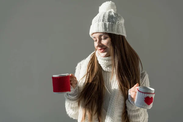 Jolie femme en pull d'hiver à la mode et écharpe tenant deux tasses isolées sur gris — Photo de stock