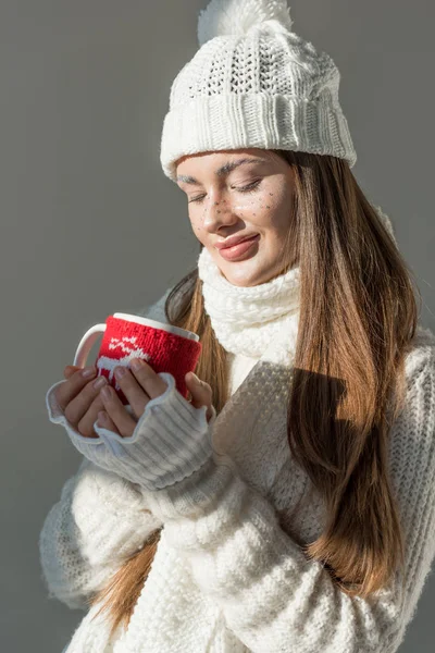 Schönes Mädchen in stylischem Winterpullover und Schal mit einer Tasse Tee isoliert auf grau — Stockfoto