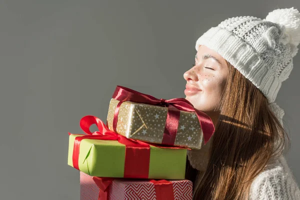 Cheerful attractive woman in fashionable winter sweater and scarf holding gift boxes isolated on grey — Stock Photo