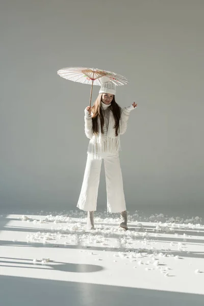 Привлекательная женщина в модном зимнем свитере и шарфе стоит с бумажным зонтиком на белом — стоковое фото