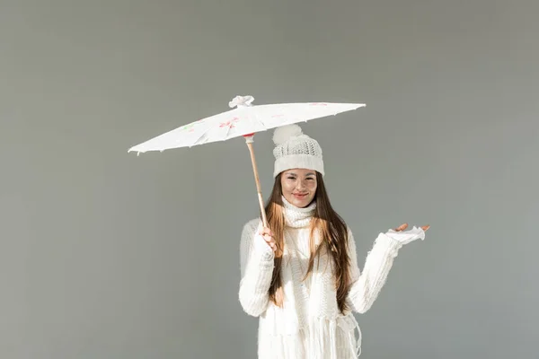 Attractive woman in fashionable winter sweater and scarf standing under paper umbrella isolated on grey — Stock Photo