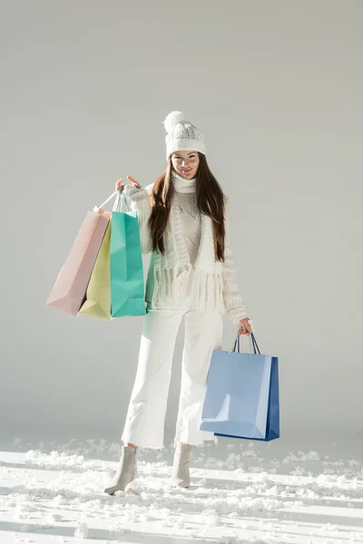 Mujer atractiva en suéter de invierno de moda y bufanda de pie con bolsas de compras y mirando a la cámara en blanco - foto de stock