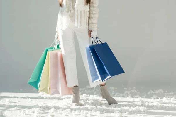 Image recadrée de la femme en pull d'hiver à la mode et écharpe debout avec des sacs à provisions sur blanc — Photo de stock