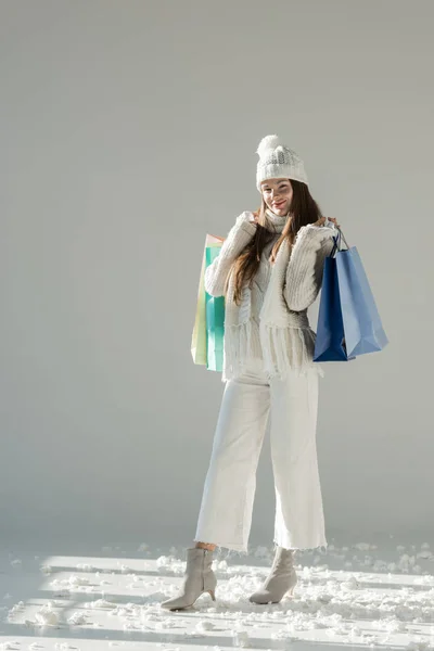 Mujer atractiva alegre en suéter de invierno elegante y bufanda de pie con bolsas de compras en blanco — Stock Photo