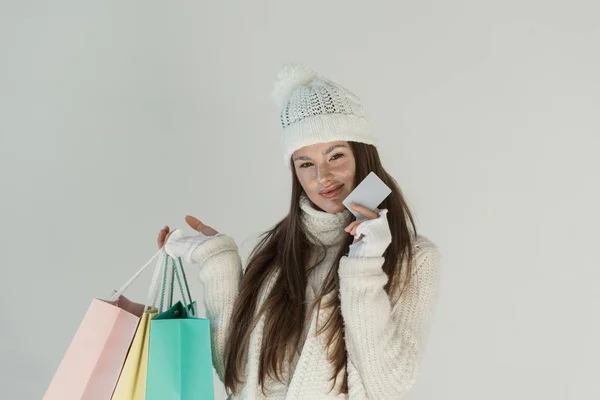 Hermosa mujer en suéter de invierno de moda y bufanda de pie con bolsas de compras y tarjeta vacía aislada en blanco - foto de stock