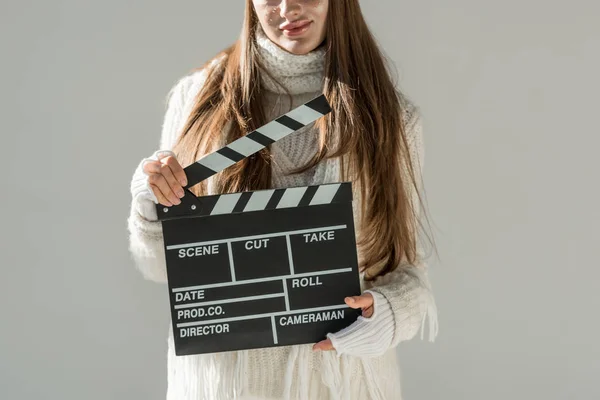 Cropped image of woman in fashionable winter sweater and scarf holding clapper board isolated on grey — Stock Photo