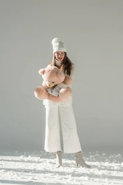 Attraktive Frau in modischem Winterpullover und Schal mit Stoffbär-Spielzeug und Blick in die Kamera auf weiß — Stockfoto