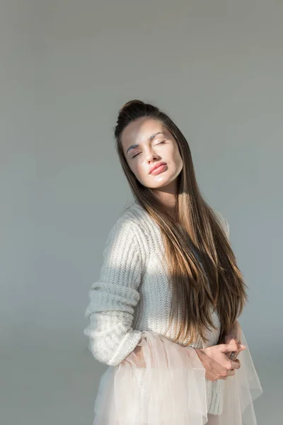 Портрет привабливої жінки в модному зимовому светрі, що стоїть з закритими очима під сонячним світлом ізольовано на білому — стокове фото