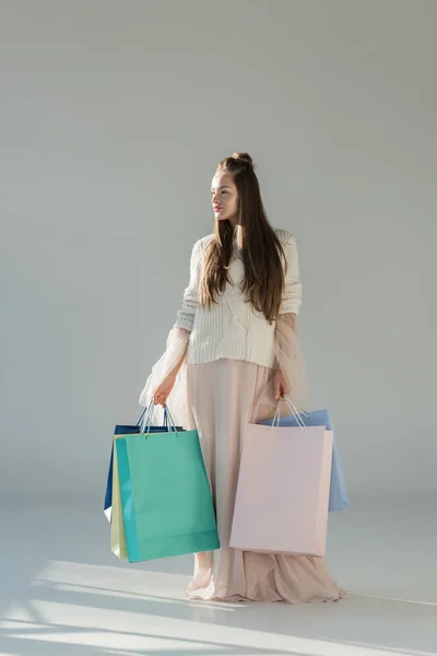 Femme attrayante en tenue d'hiver à la mode debout avec des sacs à provisions et regardant loin sur blanc — Photo de stock