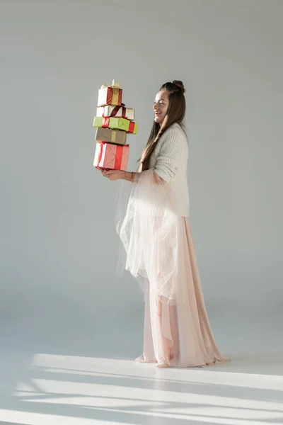 Sorrindo mulher atraente na roupa de inverno elegante segurando caixas de presente no branco — Fotografia de Stock