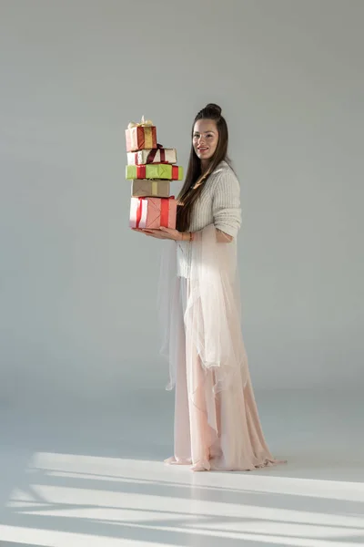 Mulher atraente na roupa de inverno elegante segurando caixas de presente e olhando para a câmera no branco — Fotografia de Stock