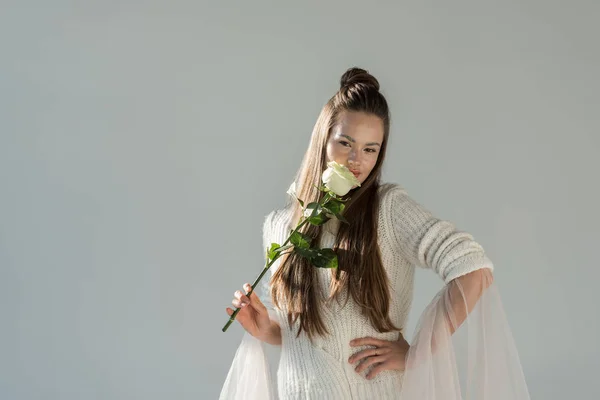 Приваблива жінка в модному зимовому вбранні нюхає білу троянду і дивиться на камеру ізольовано на білому — стокове фото