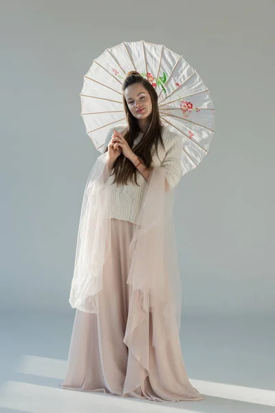 Красивая девушка в модном зимнем наряде стоит с японским зонтиком на белом — стоковое фото