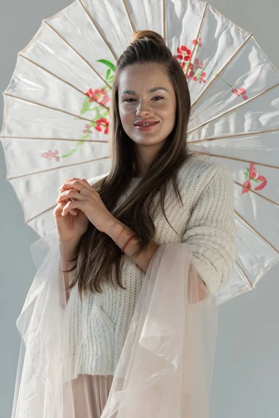 Portrait of attractive woman in fashionable winter outfit standing with paper umbrella and looking at camera on white — Stock Photo