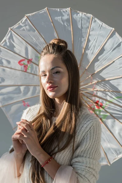 Portrait beautiful woman in stylish winter outfit standing with paper umbrella and looking at camera on white — Stock Photo