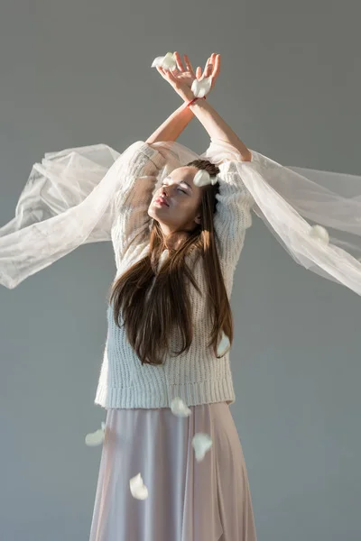 Jolie femme en tenue d'hiver à la mode debout avec les yeux fermés sous les pétales tombants isolé sur gris — Photo de stock