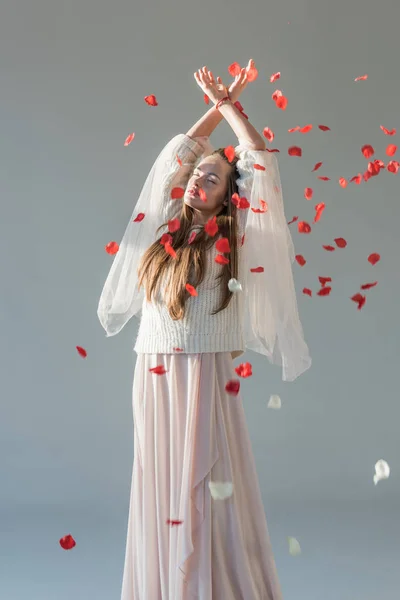 Красива жінка в стильному зимовому вбранні, що стоїть під падінням пелюсток червоних троянд ізольовані на білому — стокове фото