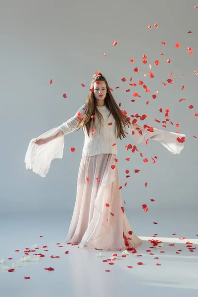 Mulher bonita na roupa de inverno na moda girando em torno de debaixo de pétalas de rosas vermelhas caindo no branco — Fotografia de Stock