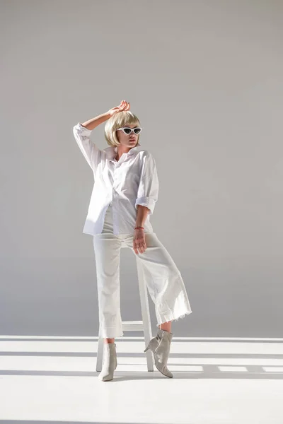 Jolie femme blonde en lunettes de soleil et tenue blanche à la mode posant sur blanc — Photo de stock