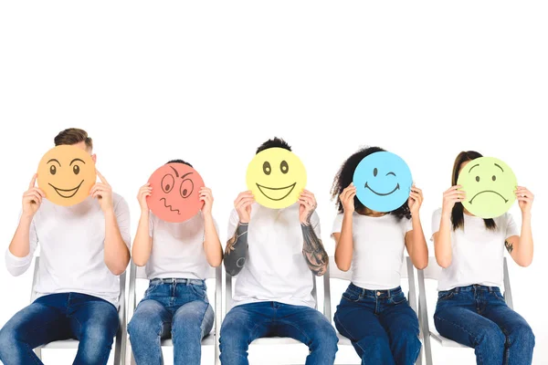 Amis multiculturels en jeans bleus assis sur des chaises et tenant des panneaux multicolores isolés sur blanc — Photo de stock