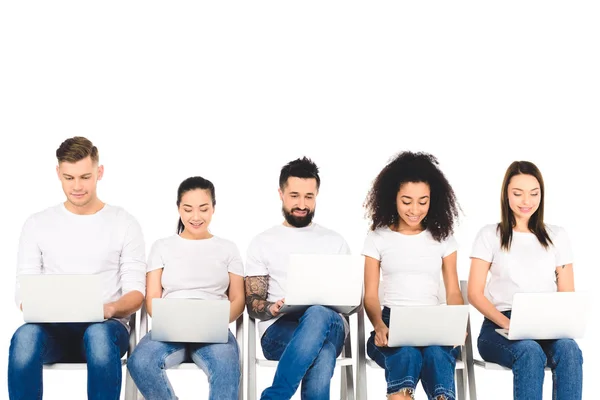 Grupo sorrindo multicultural de jovens usando laptops isolados em branco — Fotografia de Stock