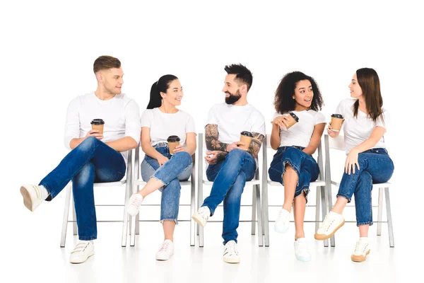 Multicultural group of people sitting on chairs with coffee to go and speaking isolated on white — Stock Photo