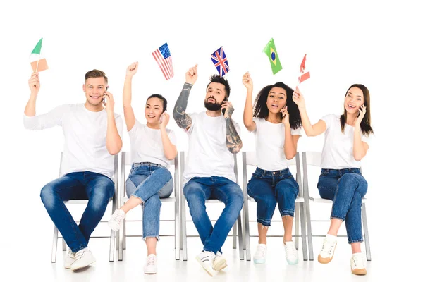 Багатоетнічна група молодих людей розмовляє по смартфонах і тримає прапори над головами ізольовані на білому — стокове фото