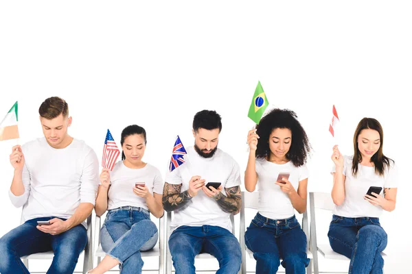 Багатоетнічна група молодих людей використовує смартфони і тримає прапори ізольовані на білому — стокове фото