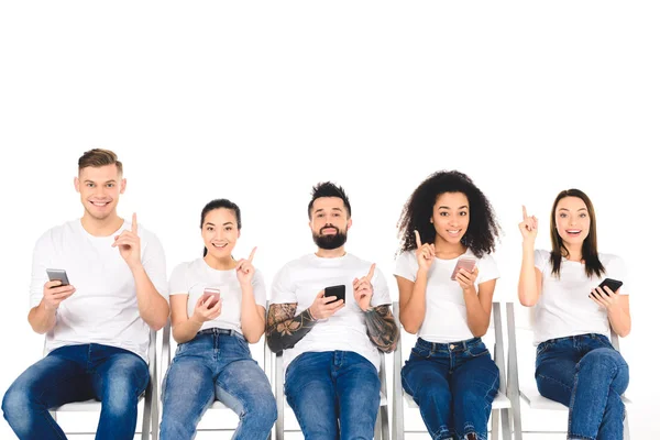Gruppo multiculturale di giovani che utilizzano smartphone e mostrano segni di idea isolati sul bianco — Foto stock