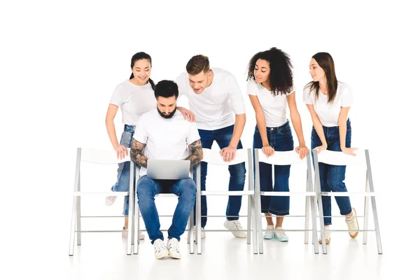 Bärtiger Mann mit Laptop, während hinter ihm eine multikulturelle Gruppe junger Leute steht und isoliert auf einen weißen Bildschirm blickt — Stockfoto