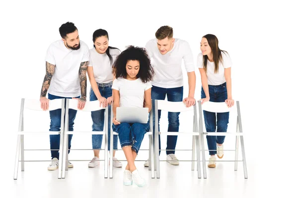 Mulher afro-americana usando laptop enquanto grupo multicultural de jovens de pé atrás e olhando para tela isolada em branco — Fotografia de Stock